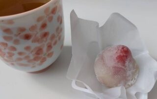Leckerer japanischer Tee in einem Becher mit japanischen Kirschblüten und einer japanischen Süßigkeit.