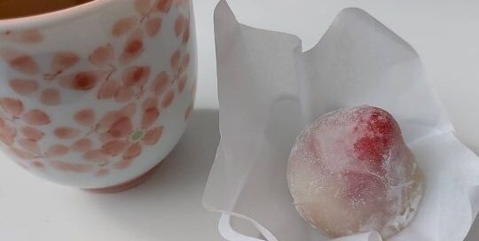 Leckerer japanischer Tee in einem Becher mit japanischen Kirschblüten und einer japanischen Süßigkeit.