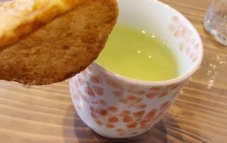 Japanischer grüner Tee mit einem Keks in einer Tasse voller japanischer Kirschblüten.