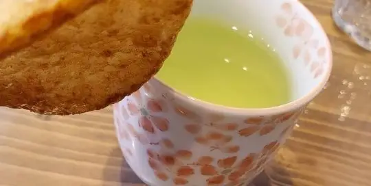 Japanischer grüner Tee mit einem Keks in einer Tasse voller japanischer Kirschblüten.